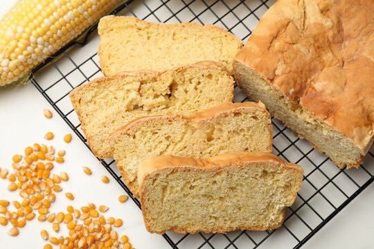 Freshly baked cut cornbread, seeds and cob on white table, flat lay