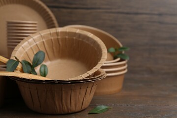 Set of disposable tableware and green leaves on wooden table, closeup. Space for text