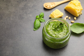 Fresh pesto sauce in jar and ingredients on grey table, closeup. Space for text