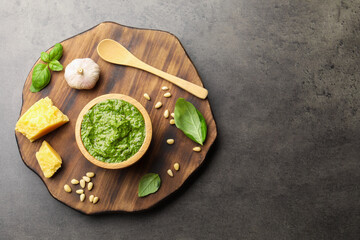 Fresh pesto sauce in bowl, spoon and ingredients on grey table, top view. Space for text