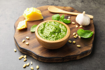 Fresh pesto sauce in bowl, spoon and ingredients on grey table, closeup