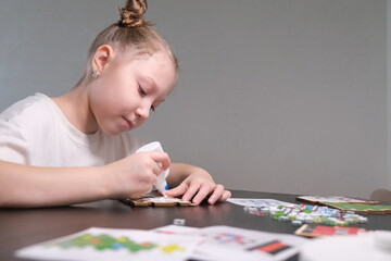 A girl makes a Christmas toy with her own hands from ceramic mosaic. Ceramic mosaic, DIY Christmas tree toy. Eco-friendly toy, educational activity for children.