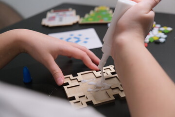 A girl makes a Christmas toy with her own hands from ceramic mosaic. Ceramic mosaic, DIY Christmas tree toy. Eco-friendly toy, educational activity for children.
