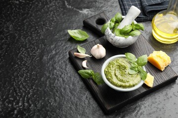 Fresh pesto sauce and ingredients on black textured table, space for text