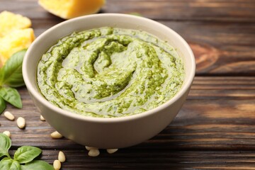 Fresh pesto sauce in bowl and ingredients on wooden table, closeup
