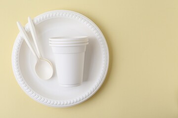 Set of disposable plastic tableware on pale yellow background, top view. Space for text