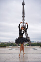 Ballerina wearing black tutu and pointe shoes performing ballet pose outdoors with the Eiffel Tower in the background in Paris, France