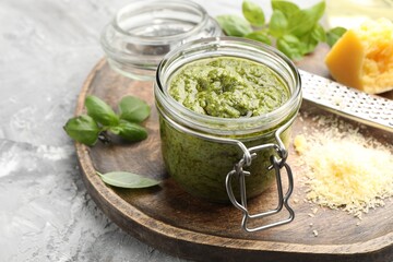 Fresh pesto sauce in jar, grater and ingredients on grey textured table, closeup
