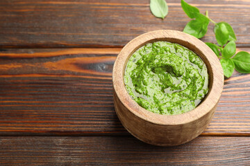 Fresh pesto sauce and basil leaves on wooden table, closeup
