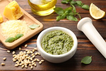 Fresh pesto sauce in mortar, pestle and ingredients on wooden table, closeup