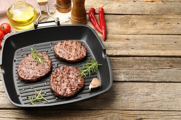 Pan with grilled patties, tomatoes and spices on wooden table, closeup. Space for text