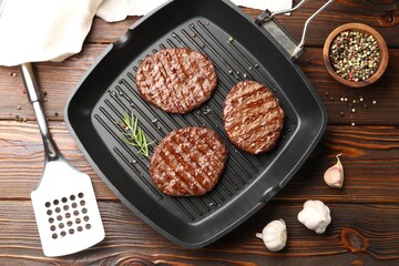 Pan with grilled patties, spices and slotted spatula on wooden table, flat lay
