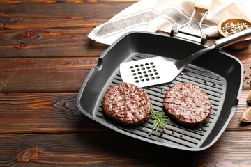 Pan with grilled patties, spices and slotted spatula on wooden table, closeup. Space for text