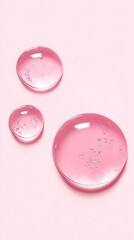 Three translucent pink droplets with delicate bubbles rest on a soft pastel background, showcasing a minimalist and serene aesthetic.