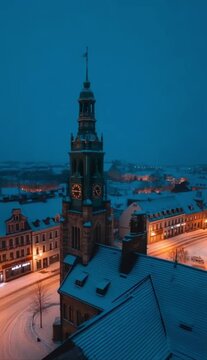 Winter night view of the town hall tower in G?strow, Germany with snow-covered roofs and streets