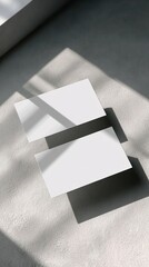 Two blank business cards resting on a textured surface, illuminated by natural light casting sharp shadows.