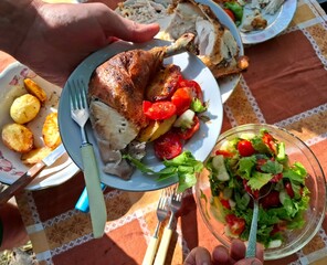 Meat and vegetables, family lunch. One person holds a plate with roasted chicken and vegetables in their hands.