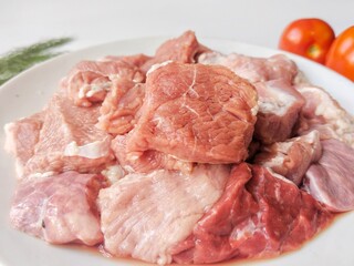 A plate of fresh, raw diced meat is shown with a tomato, dill, and kaffir lime leaves in the background.