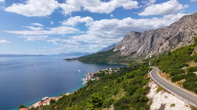 Wide aerial perspective of Drasnice and Podgora coastline emerald sea boats traces mountainous backdrop and winding D8 highway