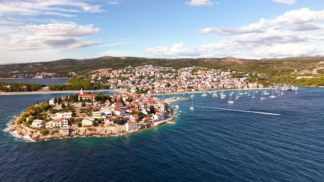 Cinematic drone panorama of Primosten Croatia peninsula old town red roofs turquoise Adriatic bay with anchored sailboats