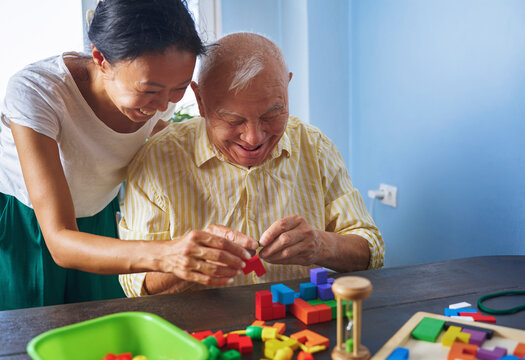 Woman helping elderly man with skill blocks during therapy indoors