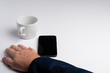 A hand resting on a table next to a smartphone and a white coffee cup