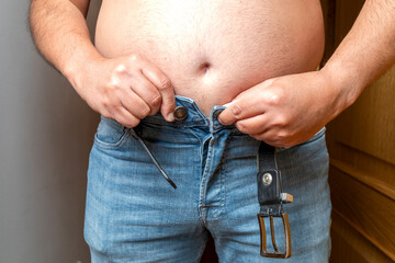 Man with an overweight belly struggling to close his tight jeans, representing weight gain and diet challenges