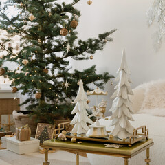 Holiday still life on a brass-trim table, two white trees and a carousel figurine with baubles and lights beside a natural Christmas tree.