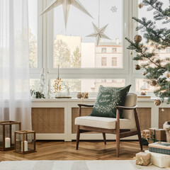 Cozy holiday corner with mid-century armchair, green cushion, Christmas tree and decorative paper stars by the window.