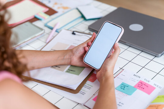 Woman using mobile phone while planning schedule at organized office desk