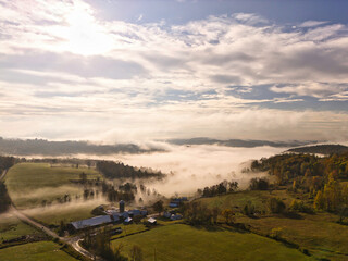 Drone aerial view of fog dissolving over a rural farm in the morning with massiv cloud formations
