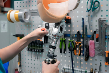 A technician works on a prosthetic leg using a screwdriver. The limb is placed on a workbench with...
