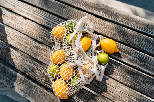 Organic lemons and limes in net bag on wooden outdoor table