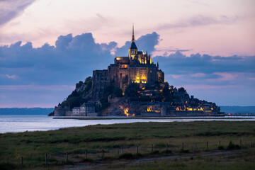 Mont Saint-Michel illuminated at dusk, rising majestically above the bay with dramatic skies and historic architecture, symbol of France&rsquo;s heritage and timeless beauty