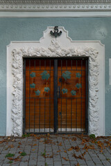 Vertical shot of a blue building wall with wooden doors featuring wrought iron grape leaf grilles,...