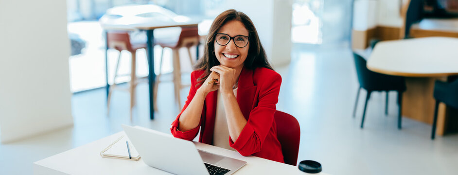 Professional woman in red blazer smiling at desk in a bright office