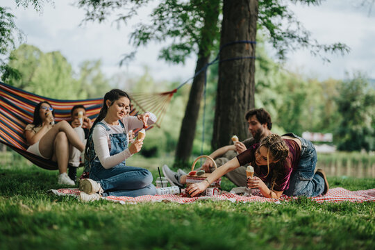 A diverse group of friends sharing a joyful and relaxed moment outdoors, enjoying a picnic and ice creams while basking in the tranquil ambiance of a vibrant park setting.