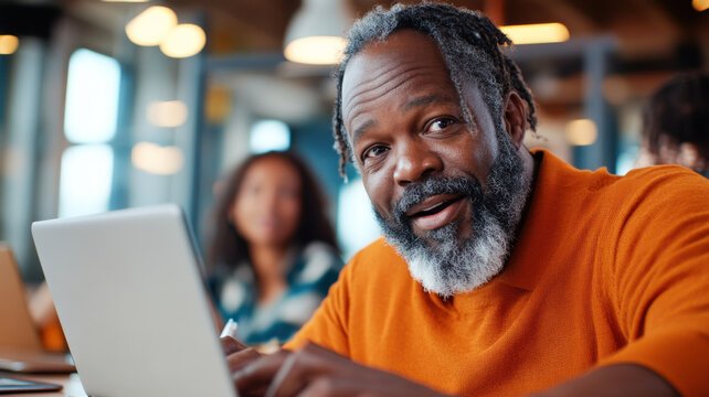 Middle-aged black man presenting survey findings from his laptop in a shared workspace with team in the background. Survey research answer checklist