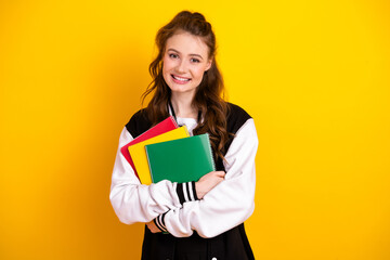 Smiling young female student holding colorful notebooks against a yellow background, symbolizing education