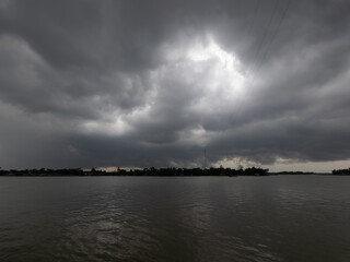 Fototapeta premium Dramatic dark storm clouds gathering over a tranquil river before a thunderstorm, creating an ominous and moody atmosphere