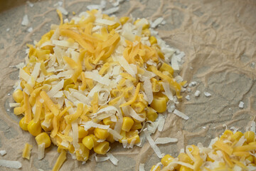 Close-up view of corn rounds on parchment paper topped with two different types of grated cheese. Texture and detail of both cheeses are clearly visible, ready for baking.