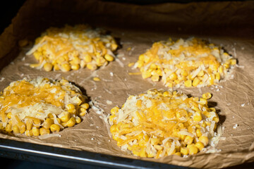 Close-up view inside the oven, highlighting corn rounds topped with cheese. Warm light illuminates the texture and color of the corn, ready to bake, cozy kitchen scene.