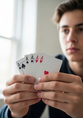 Teenager holding four aces playing card in his hand close to window