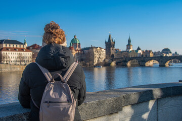 A woman with a backpack enjoys the view of the Charles Bridge and the Vltava River