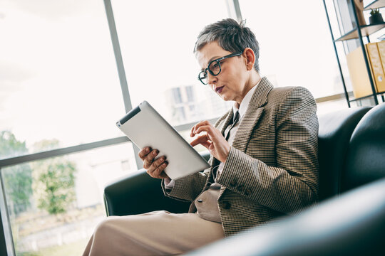 Confident businesswoman working attentively in a modern office setting, using a tablet for professional tasks and analysis - Powered by Adobe