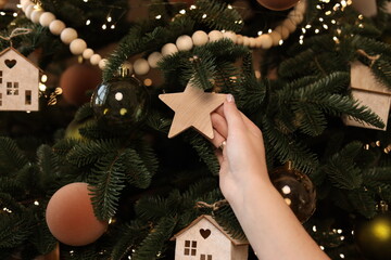 A hand holds a wooden star ornament as it prepares to be placed on a beautifully decorated...
