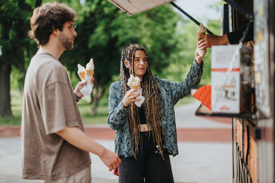 A group of friends purchasing and savoring ice cream outdoors surrounded by greenery and sunlight. - Powered by Adobe