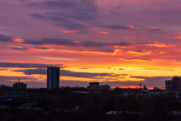 Naklejka premium A vibrant sunset over a city skyline. The sky is filled with shades of orange, pink, and purple. Silhouettes of buildings are visible against the colorful backdrop.