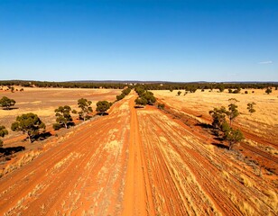 Red dirt road stretches across a vast, arid landscape under a vibrant blue sky