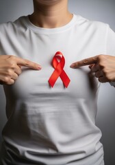 Young woman pointing at red ribbon on her chest for world aids day awareness